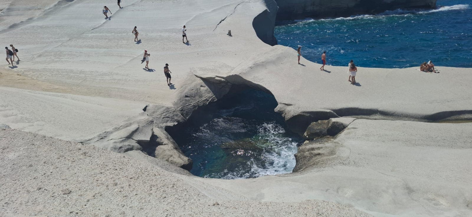 Visitors around the sea-cave swimming hole in the lunar white landscape of Sarakiniko, Milos